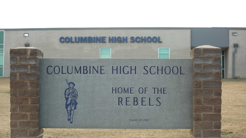 The exterior of Columbine High School is seen, with an engraving that reads, 'Home of Rebels'.