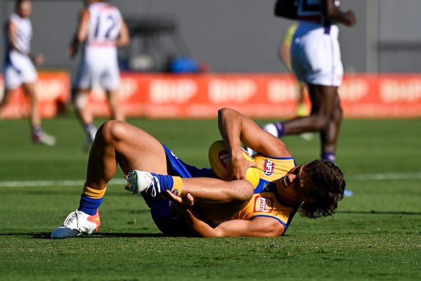 Campbell Chesser lies on the ground and clutches at his foot while holding the football