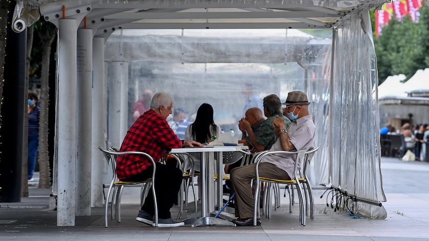 People wearing face masks sit at an undercover outdoor table.