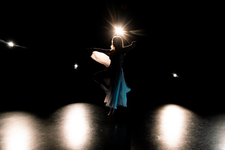 the silhouette of a woman dancing on a stage with bright lights behind her