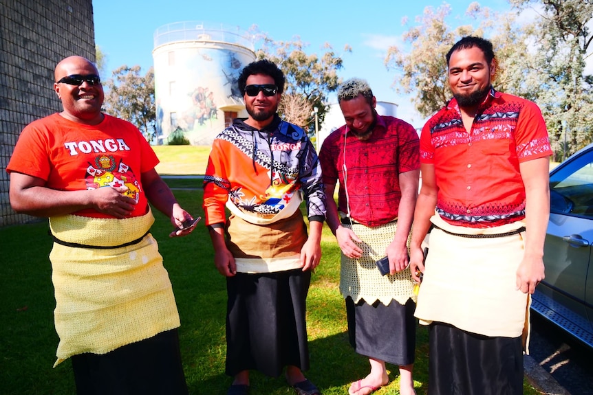 Four Tongan men stand in red shirts.