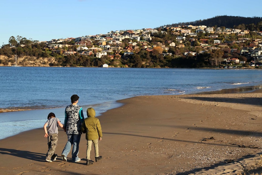 Unidentified family members walk on beach at Blackmans Bay, Hobart.
