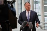 Energy and Environment Minister Josh Frydenberg speaks to the media in Parliament House, wearing a navy suit and striped tie.