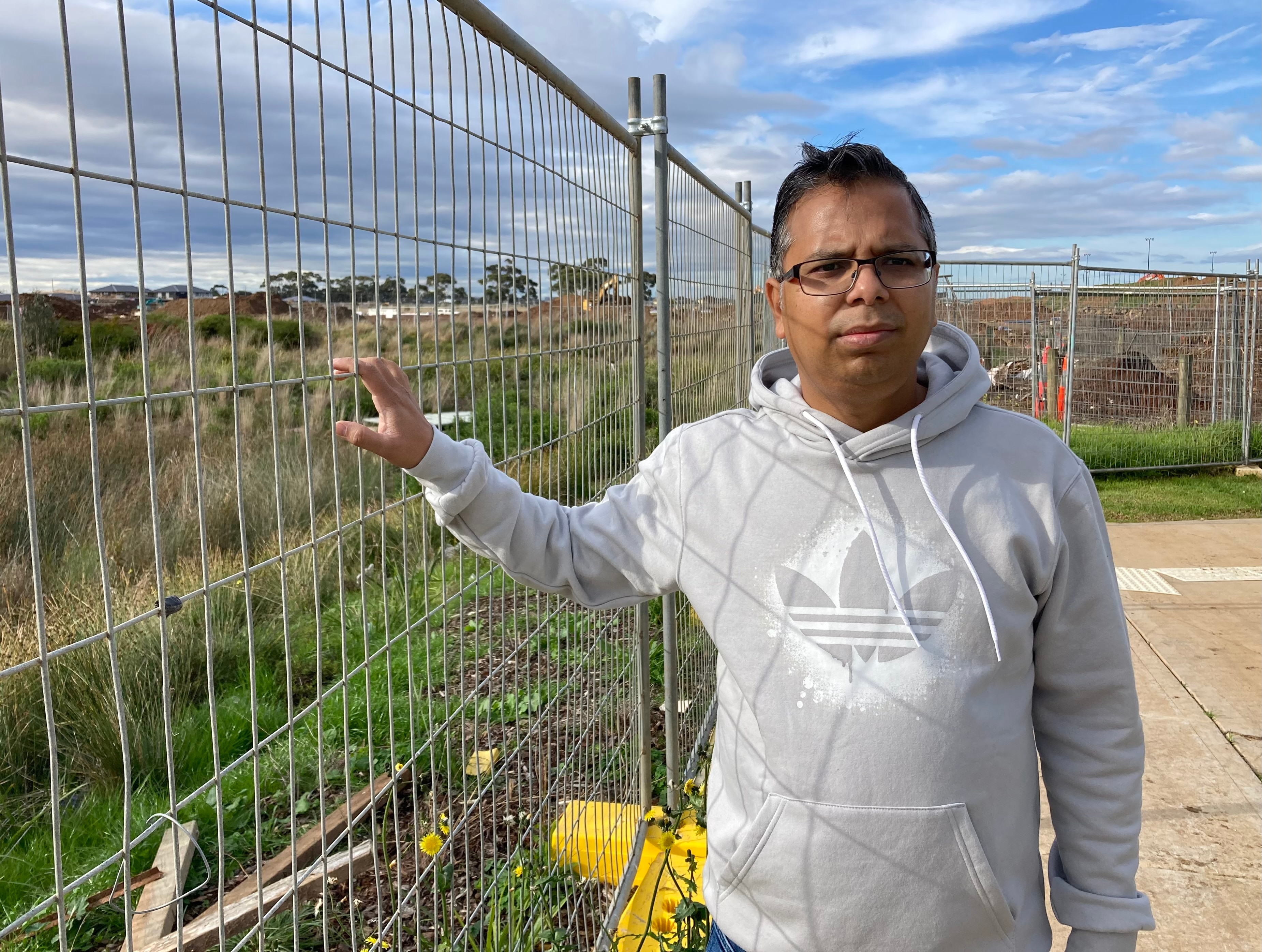 A man standing next to a metal fence on vacant land