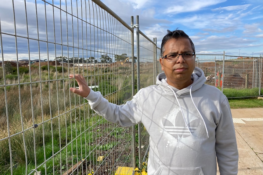 A man standing next to a metal fence on vacant land