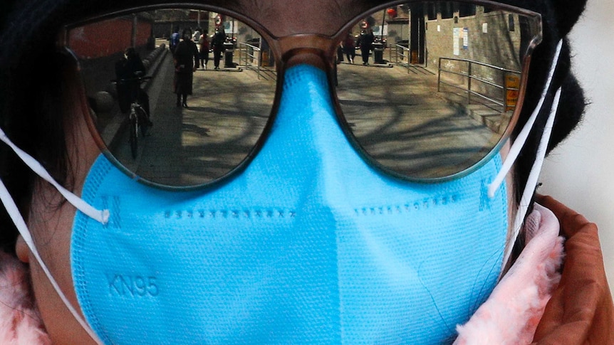 People are reflected in a man's sunglasses, he is wearing a mask, as many of them are.