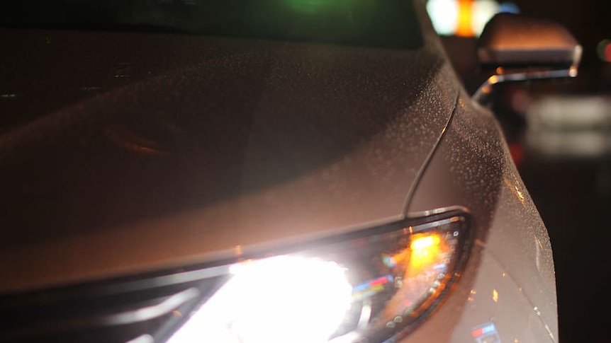 A close up of a silver car with its lights on at night.