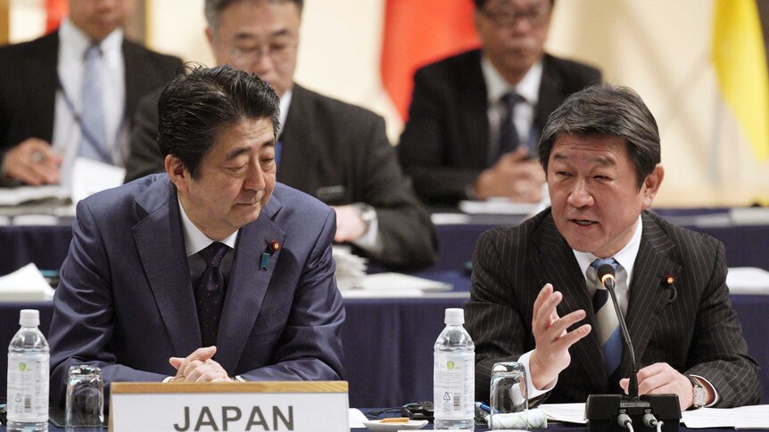 Shinzo Abe sits next to Japan's Minister of economy at a table with a placard on it that says Japan