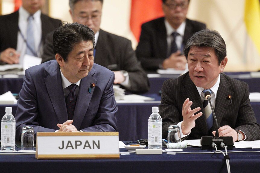 Shinzo Abe sits next to Japan's Minister of economy at a table with a placard on it that says Japan