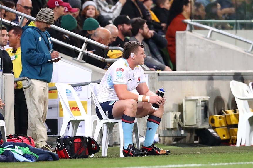 A NSW Waratahs Super Rugby Pacific player sits on a chair on the sideline.