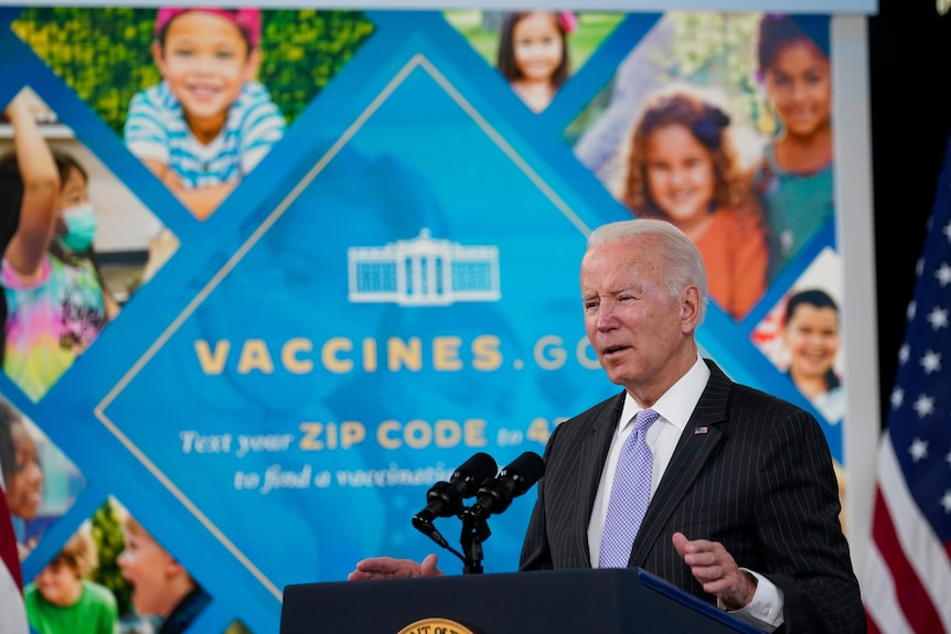 US President Joe Biden stands at a podium in front of a banner reading vaccines.gov