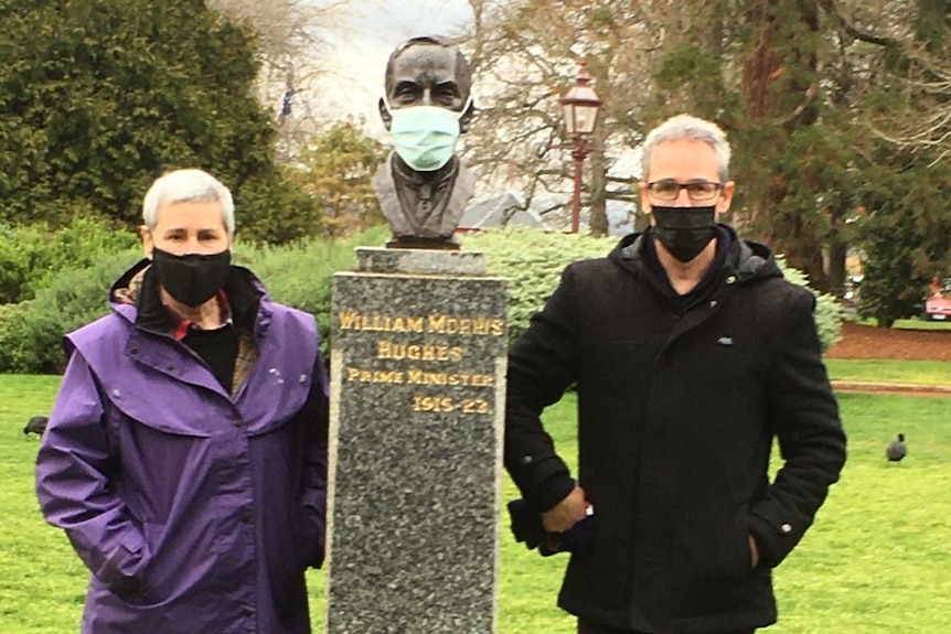a woman and man stand with a sculpture of a Prime Minister in Ballarat, all wearing masks