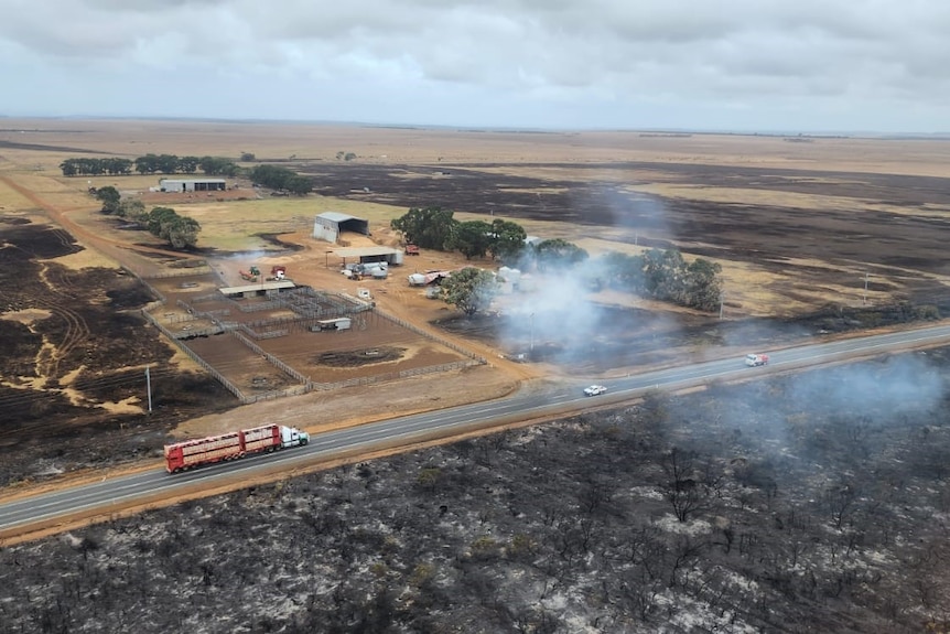 Smoke rises off burnt paddocks near a highway, as seen from above.