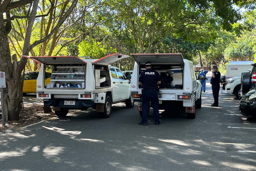 Queensland Police officers stand near vehicles at crime scene