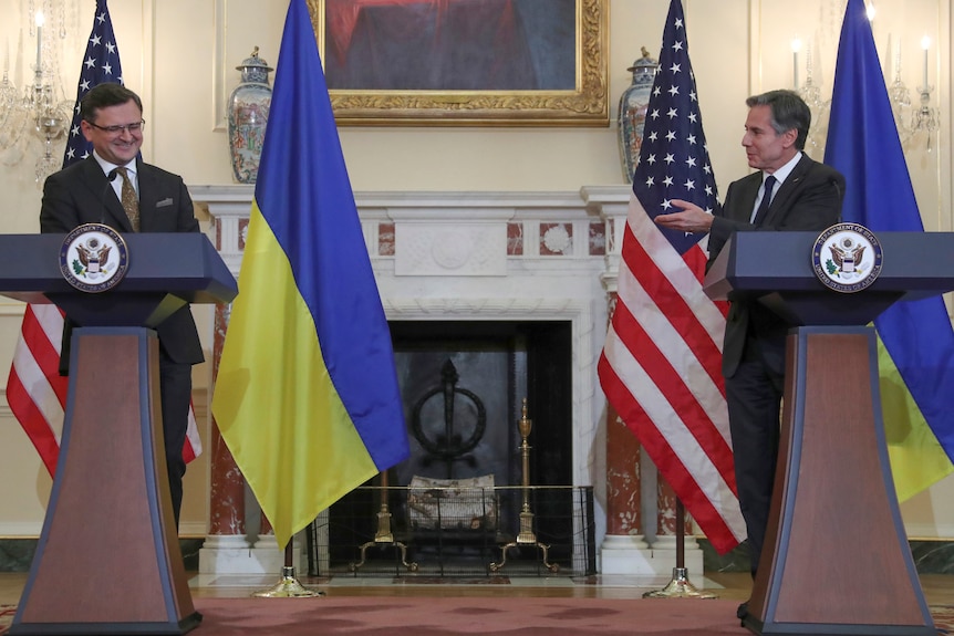 Two politicans in suits stand behind podiums during a press conference. 