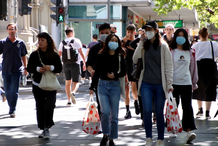 People walk through Melbourne's CBD, some of whom are wearing face masks.