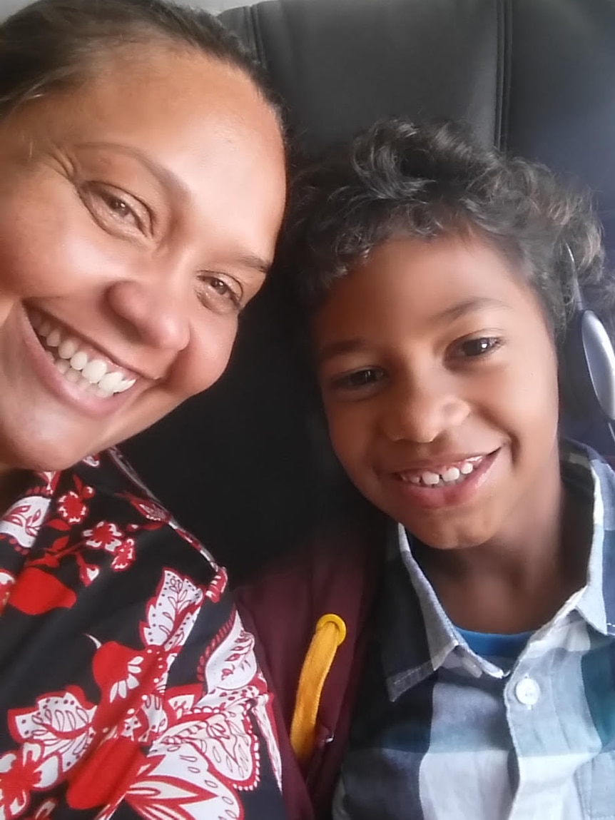 A smartphone self-portrait shows a mother and child in an airplane seat smiling and looking into the camera.