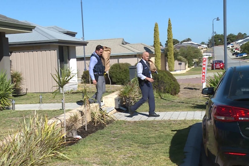 Two police officers walk outside a home in suburban Perth, carrying a large paper bag each.