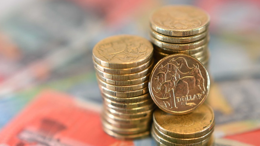 A pile of dollar coins sits on bank notes on a edesk.