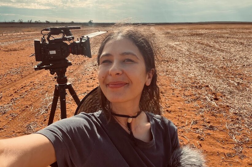 A women with dark hair takes a selfie in a country area.