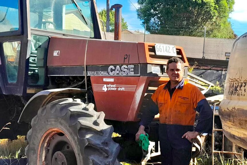 Middle aged man in high-vis stands in front of tractor, hand on hip