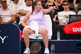 An angry tennis player sits in her chair at a change of ends, as she points her finger towards the umpire (out of shot). 