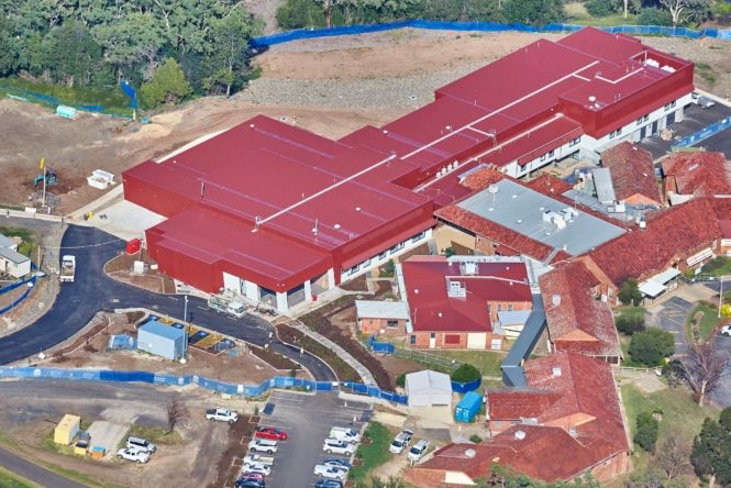 A view from above of a large building under construction with a red roof, roads around the outside, and trees.