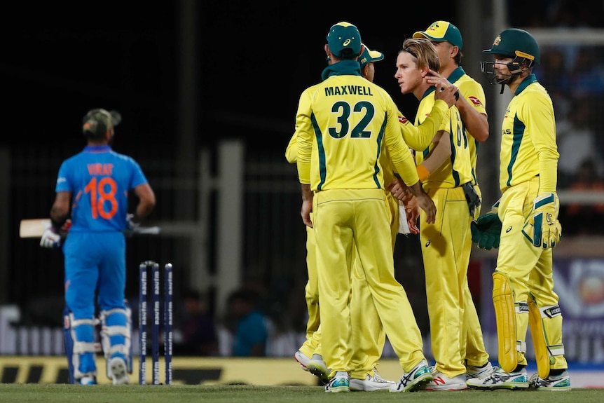 A group of five Australian cricketers celebrate as India's Virat Kohli walks off the ground