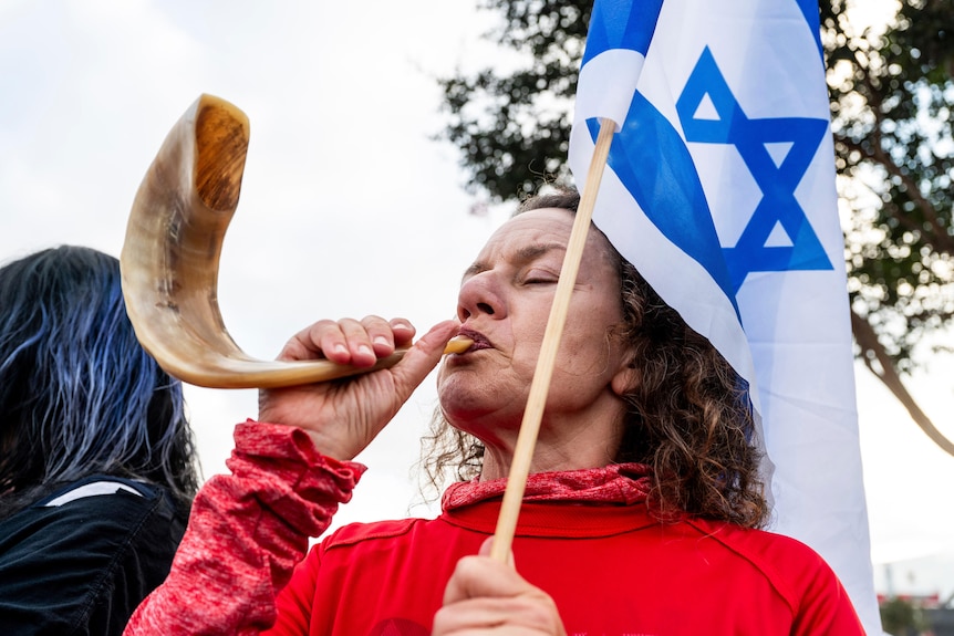 A woman blows into a horn holding a blue and white flag.