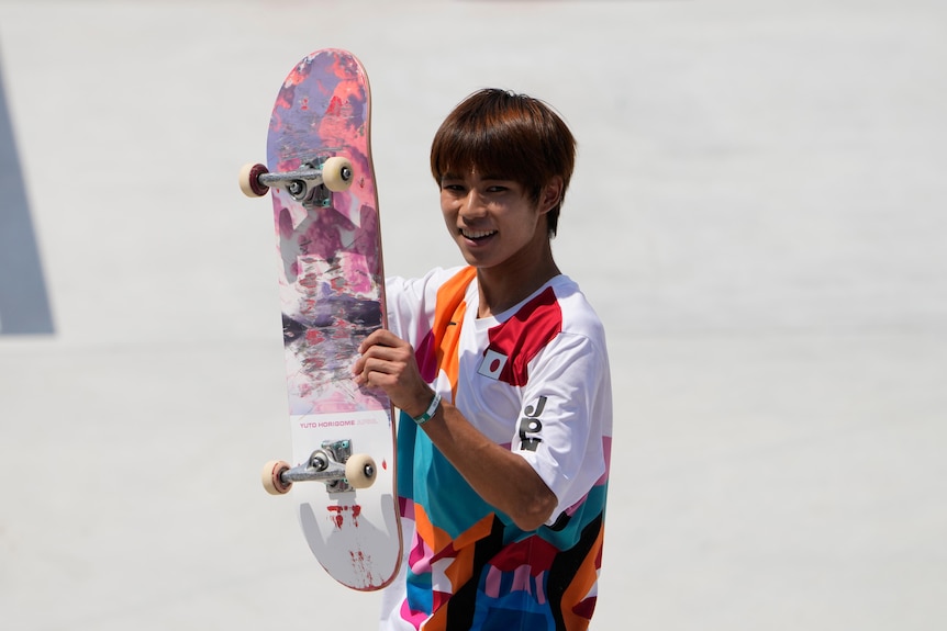 A Japanese skateboarder lifts his skateboard at the Tokyo Olympics.