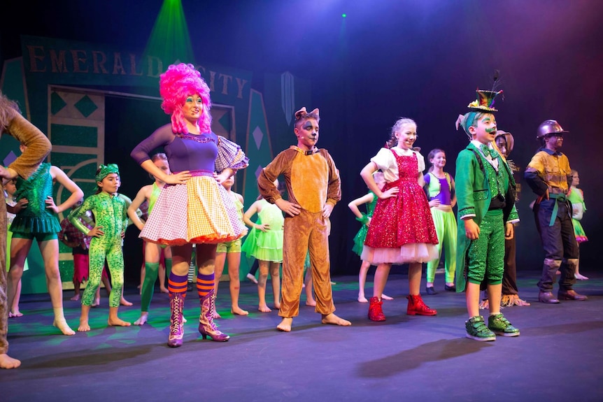 A group of young actors on stage performing in colourful costumes