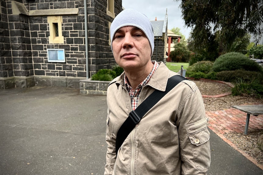 A man wears a beanie and side bag while standing outside a parish