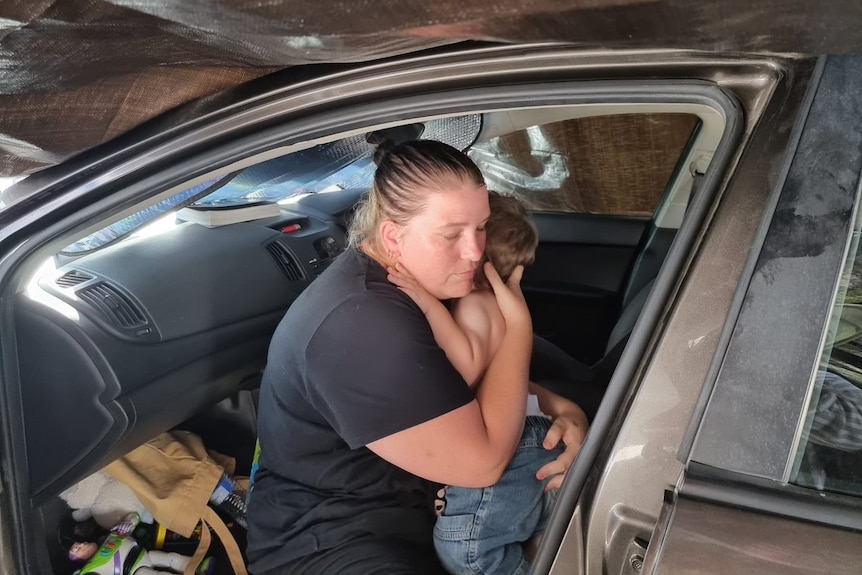 A mother hugs her son in the front seat of her car. 