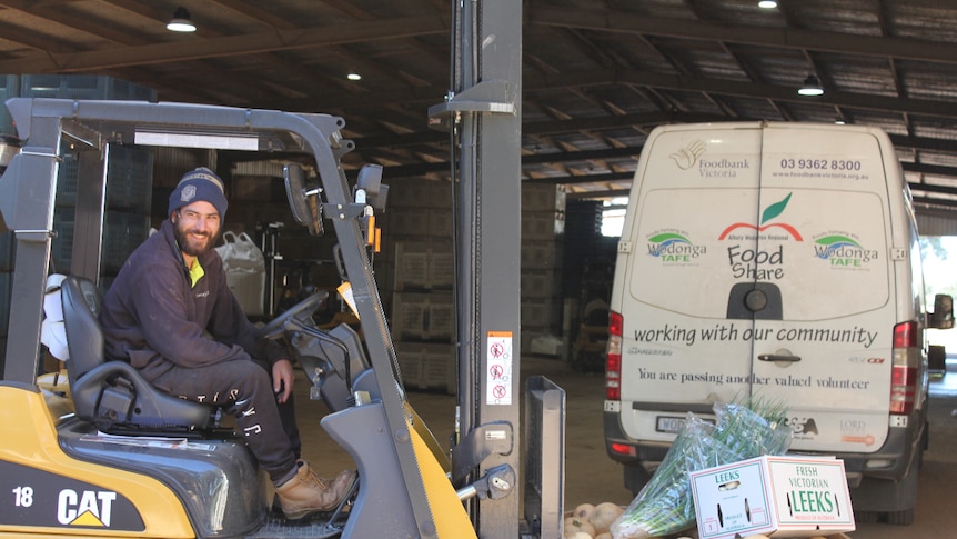 Farmer sits on forklift carrying a bin of donated fresh produce. FoodShare van is in the background.