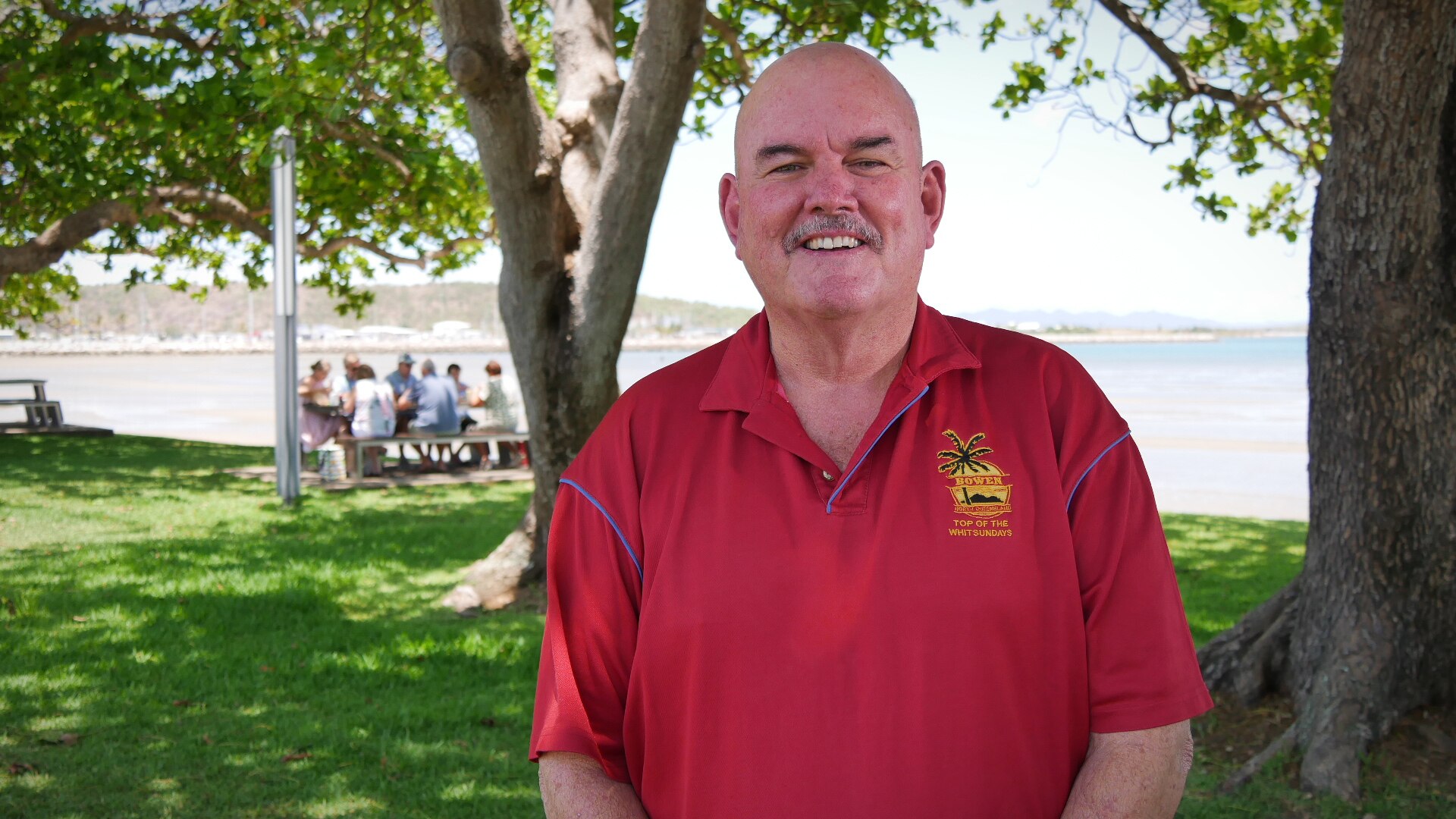 A man smiles while standing in a waterfront park