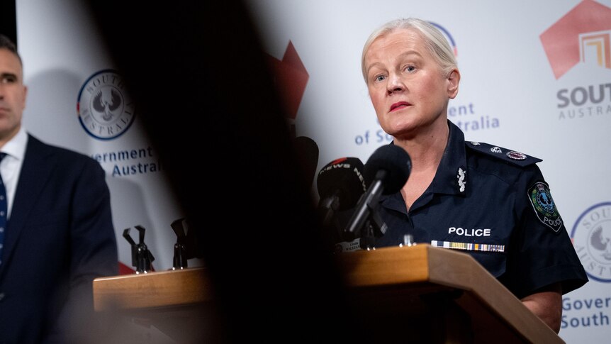A woman with light blonde hair wearing a police uniform speaking at a press conference.