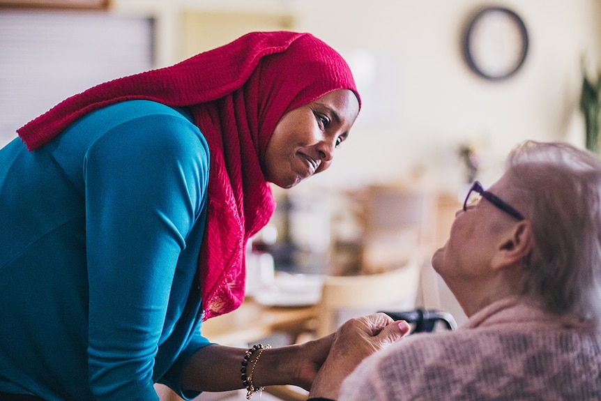 A woman wearing a headscarf holding the hand of an elderly woman.