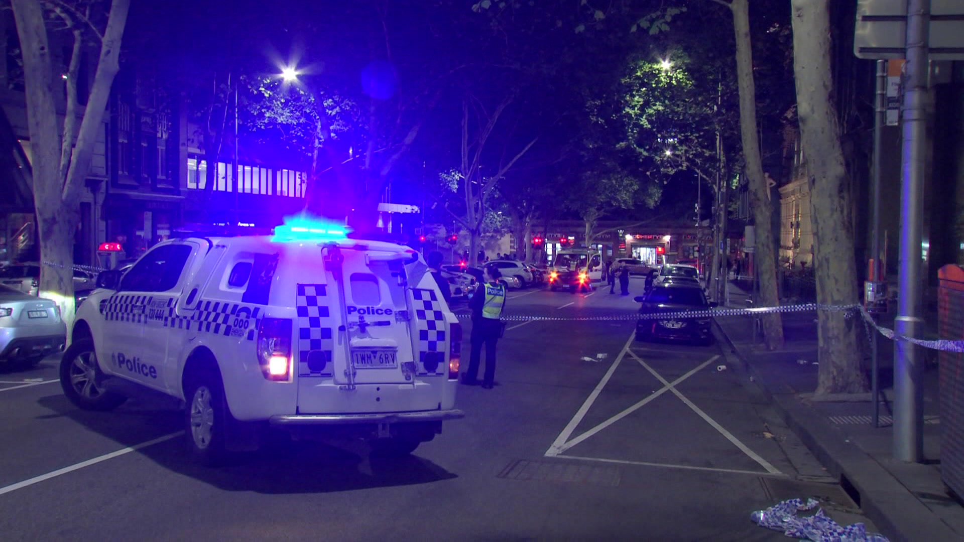 Un oficial de policía se encuentra cerca de un coche de policía y un cordón policial que bloquea una calle del centro por la noche.