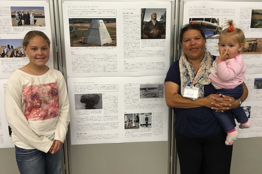 Karina Lester stands in front of her presentation  in Hiroshima with her daughters.