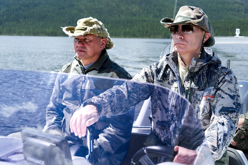 Putin and Shoigu in camo gear driving a boat