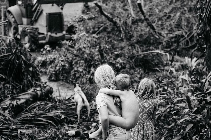 Three children and a dog watch on as a bulldozer enters their land