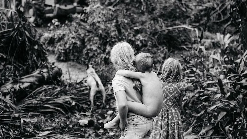 Three children and a dog watch on as a bulldozer enters their land