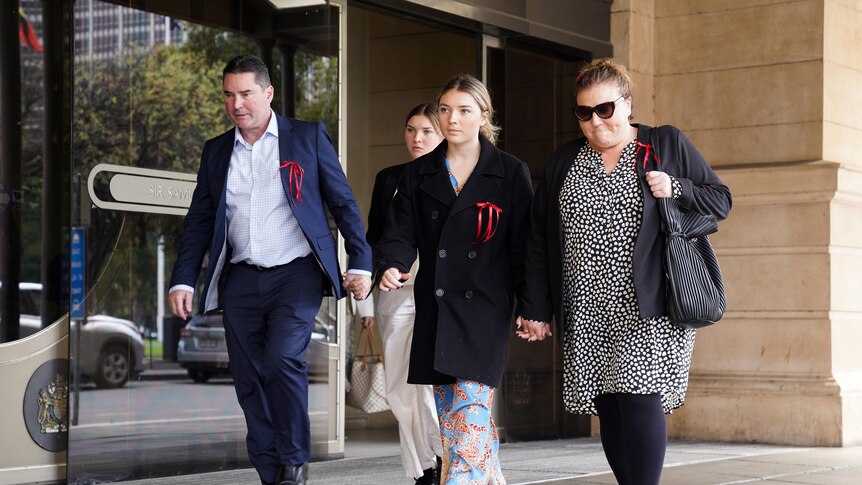 A man, two girls and a woman, all wearing red ribbons, walk outside court building