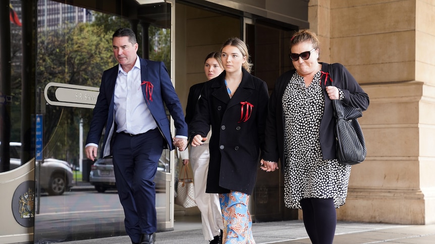 A man, two girls and a woman, all wearing red ribbons, walk outside court building