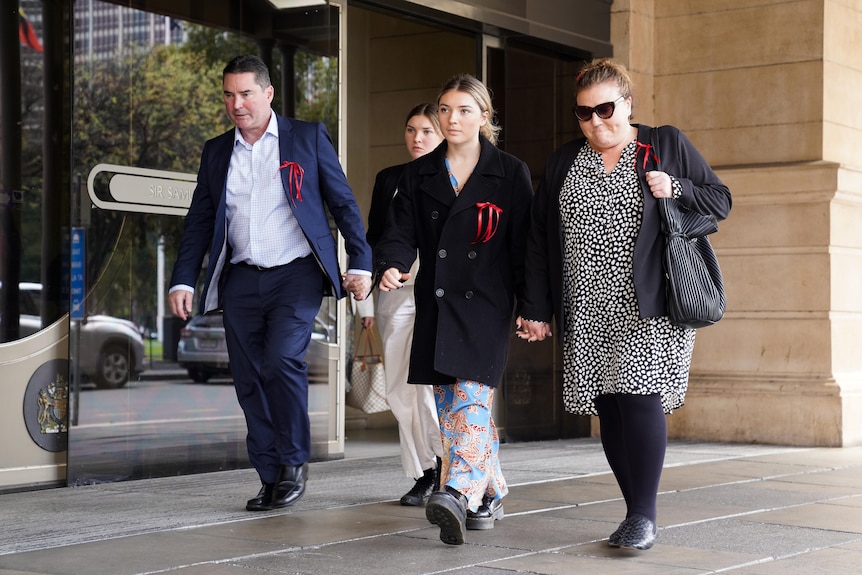 A man, two girls and a woman, all wearing red ribbons, walk outside court building