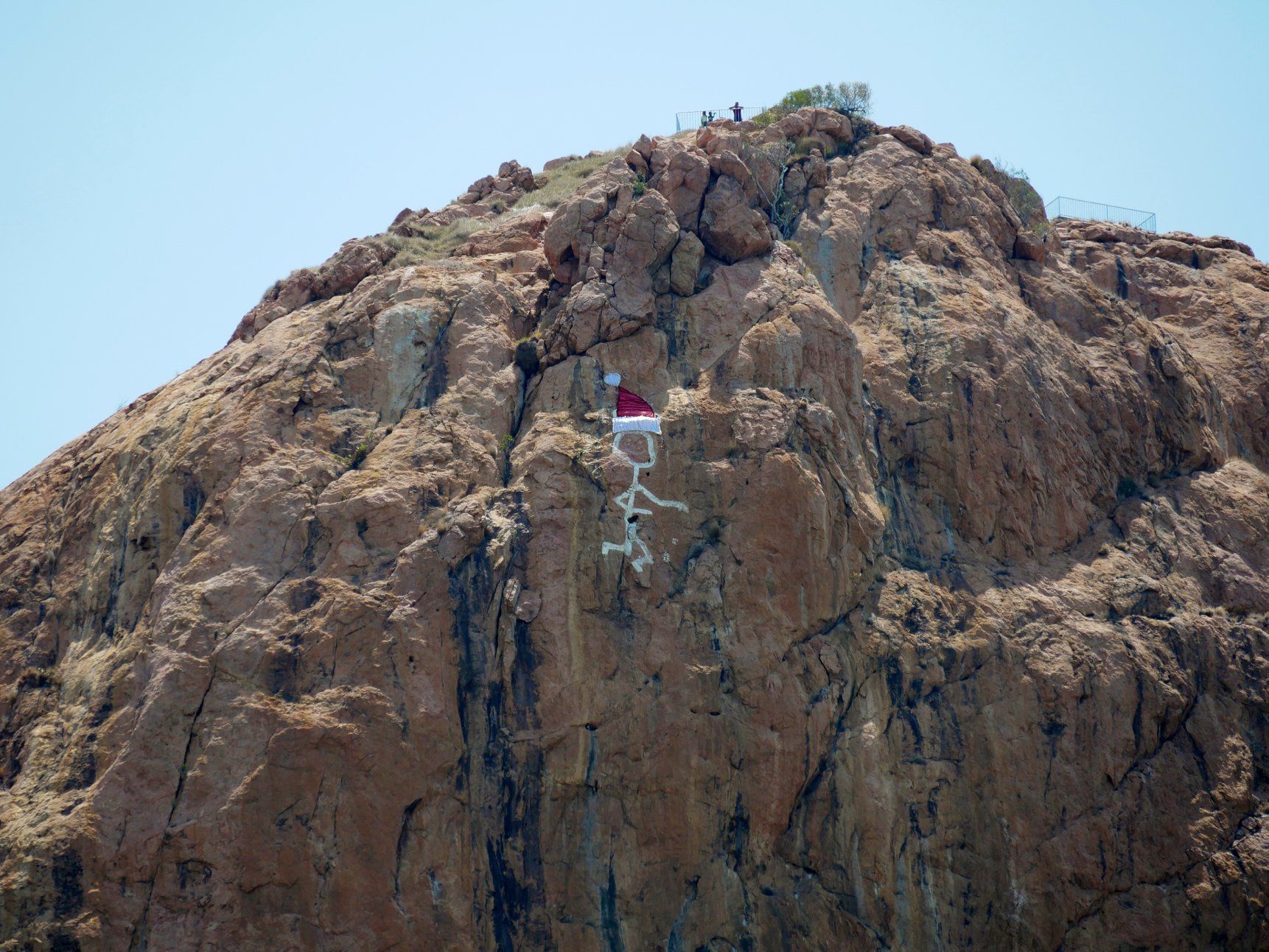 A 'saintly' figure painted in white on the side of a rock face with a red santa clause hat painted