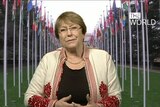 A still of UN rights chief Michelle Bachelet with world flags hanging in the background.