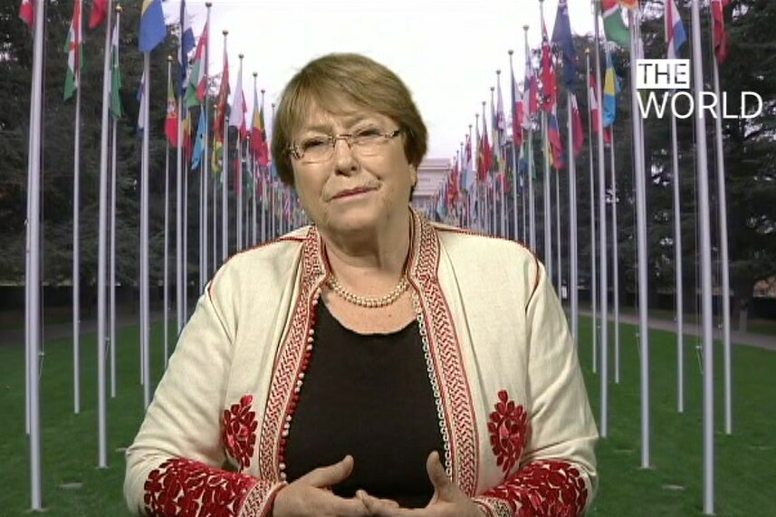 A still of UN rights chief Michelle Bachelet with world flags hanging in the background.