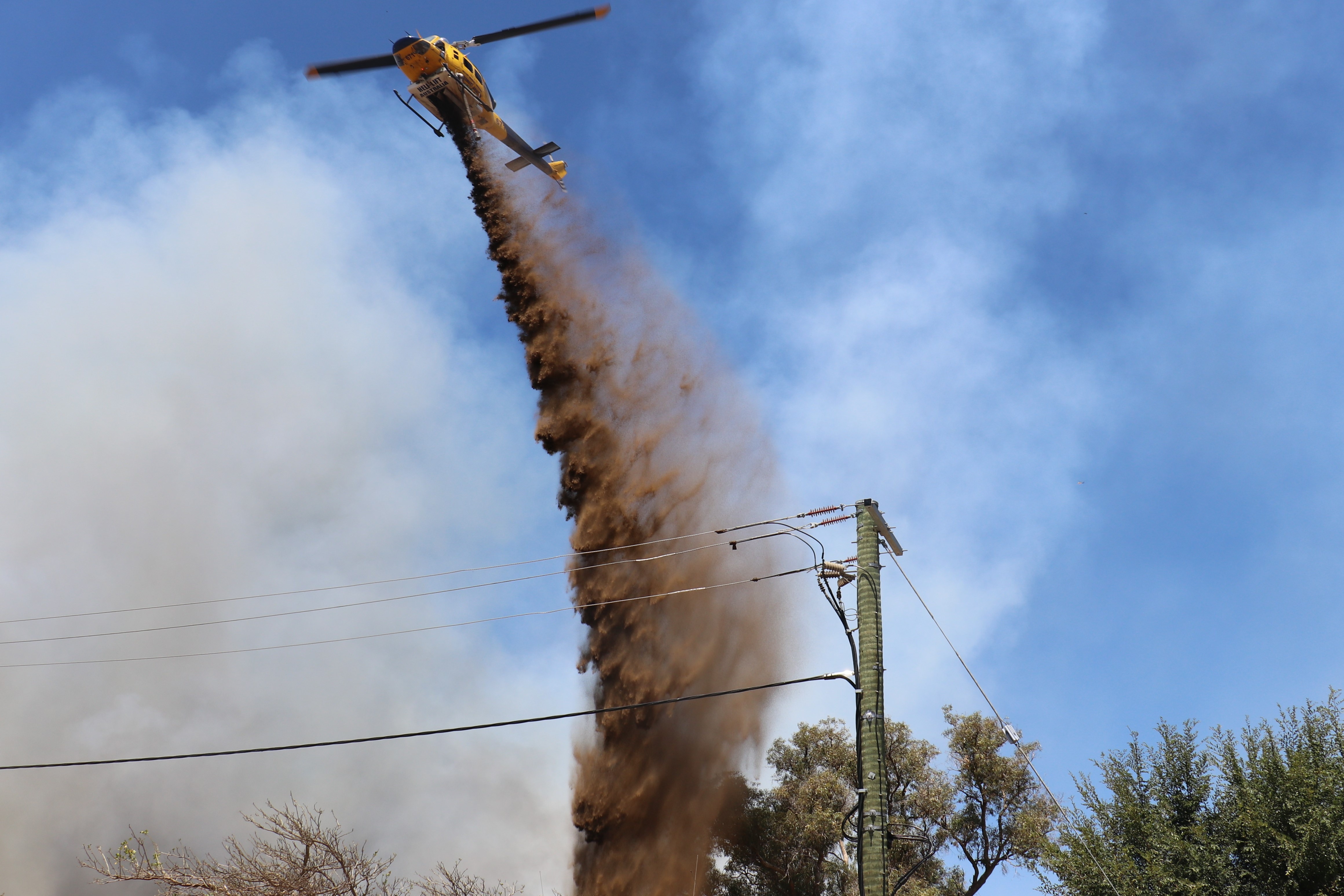 Um helicóptero lança retardante em arbustos em chamas.