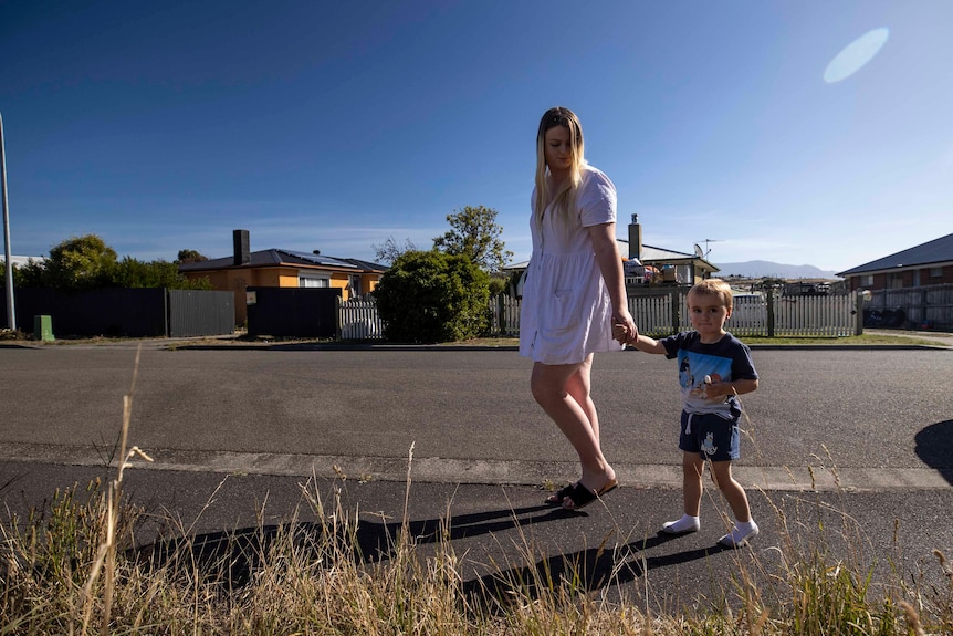 A woman walks along a suburban footpath with her young son.